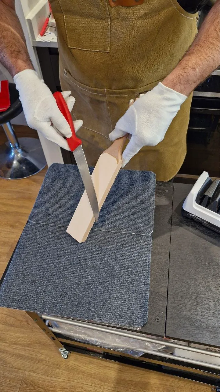 Gloved hands honing a kitchen knife on a leather strop at the mobile workshop table