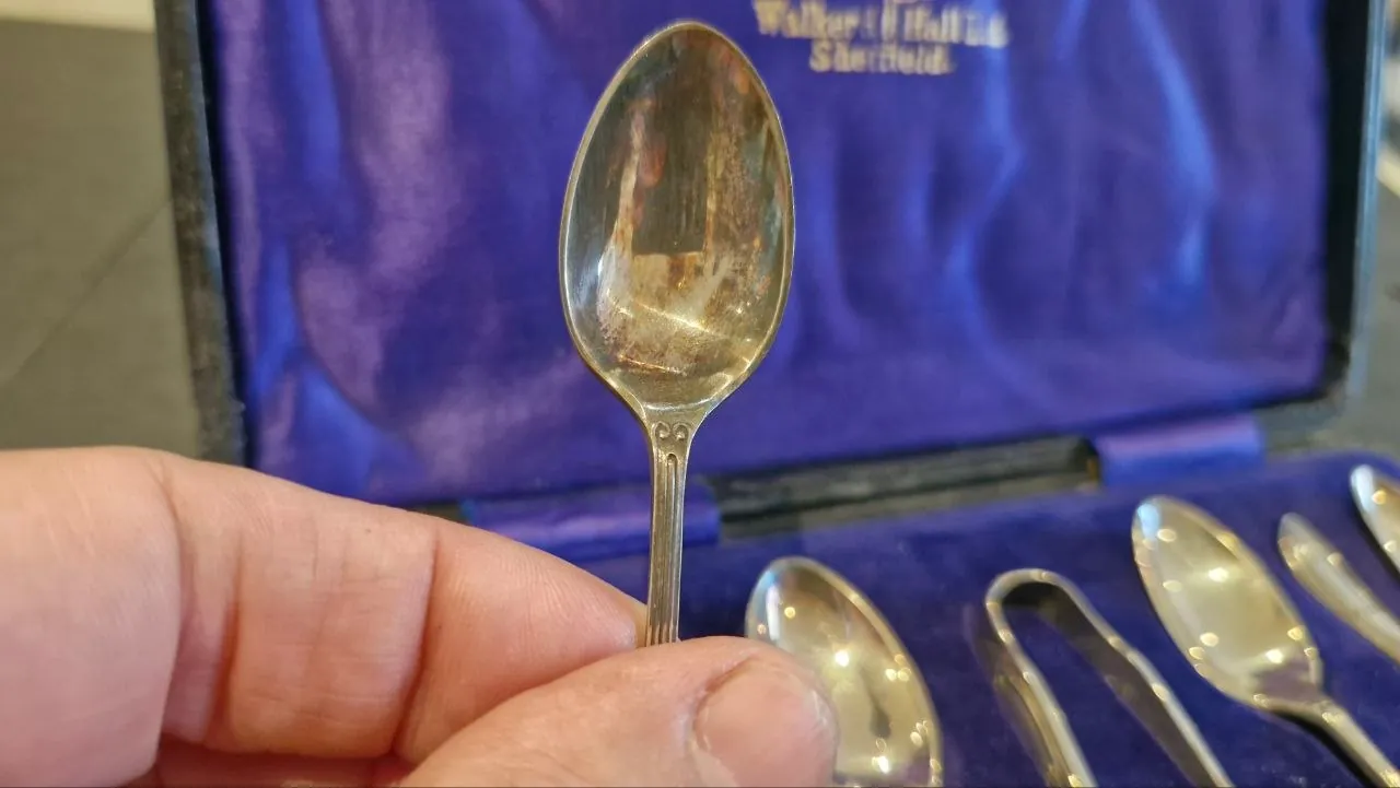 A tarnished Walker & Hall Sheffield teaspoon held up before restoration, the rest of the cased set behind it