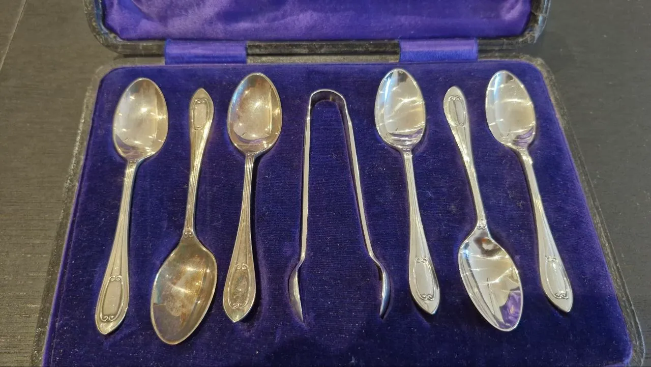A Walker & Hall teaspoon set halfway through restoration: two tarnished spoons beside bright, restored ones in the purple velvet case